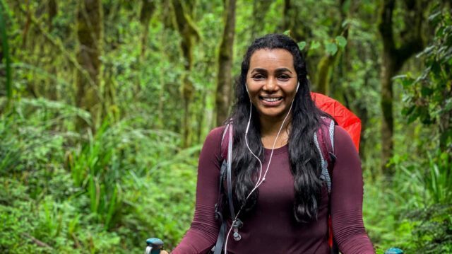 Life Happens Outdoors climber trekking through Kilimanjaro’s rainforest on day one of the Machame Route, smiling en route to Machame Camp.