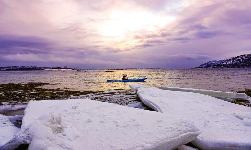 Life Happens Outdoors team member kayaking beside blocks of ice on frozen fjords during a Norway northern lights adventure tour