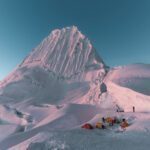 Tents on a snowy plateau beneath Alpamayo’s fluted face in Peru.