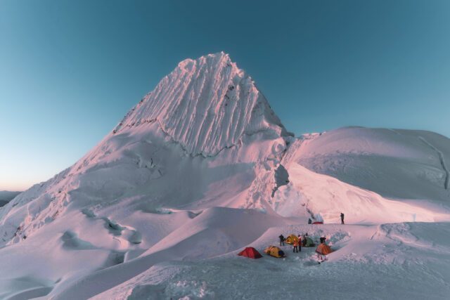 Tents on a snowy plateau beneath Alpamayo’s fluted face in Peru.