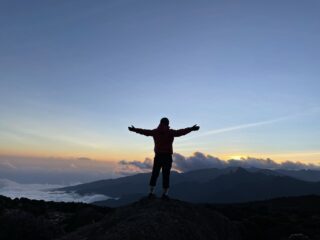 Trekker stands with arms outstretched above the clouds at sunrise on Mount Kilimanjaro.