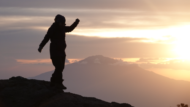 Life Happens Outdoors climber at Karanga Camp on Mount Kilimanjaro, watching a breathtaking sunset with Mount Meru in the distance.