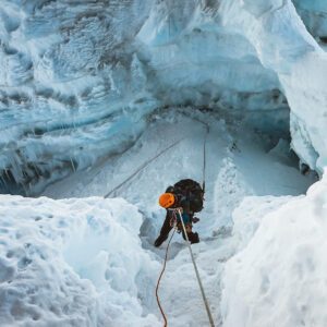 Climber descending between towering glacier walls on an abseil, surrounded by shimmering ice formations on the Island.
