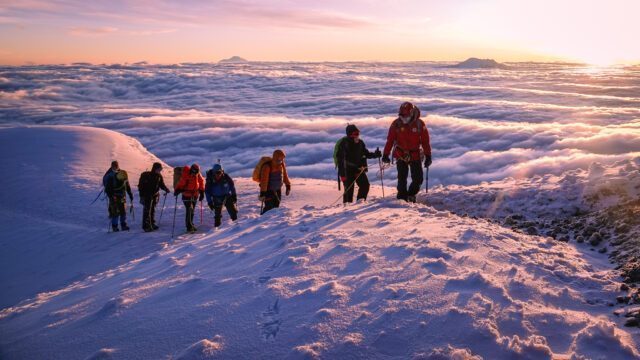 The Life Happens Outdoors team and protagonists of "The Summit Within: A Journey to the Furthest Point on Earth" on the shoulder of Cotopaxi at sunrise, with a sea of clouds below and the giant volcanoes of Ecuador dotting the skyline. The team is led by LHO IFMGA guide Franklin Varela.
