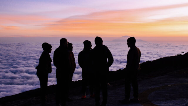Life Happens Outdoors team at Shira Camp on Kilimanjaro, watching a vivid purple sunset above a sea of clouds on the Machame Route.