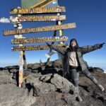 LHOer next to the summit sign of Uhuru Peak on Kilimanjaro at 5,895 meters in great weather with no snow during the Climb Kilimanjaro Expedition with the Life Happens Outdoors team.