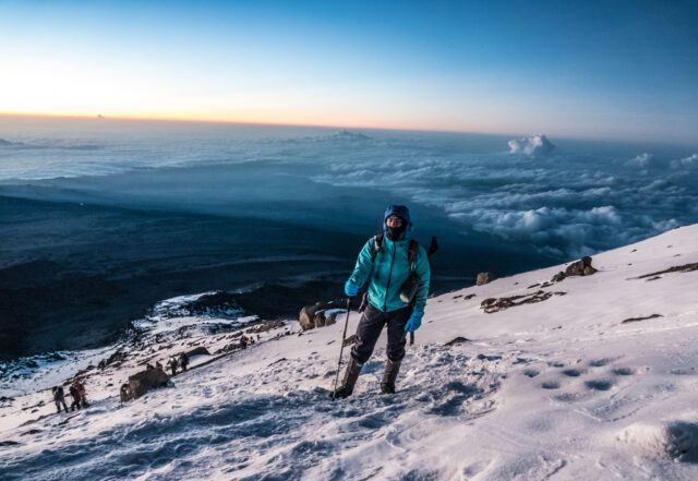 LHOer Omran Antar at sunrise just below Stella Point, with a beautiful purple sky and a sea of clouds covering the savannah plains during the Climb Kilimanjaro Expedition with the Life Happens Outdoors team.