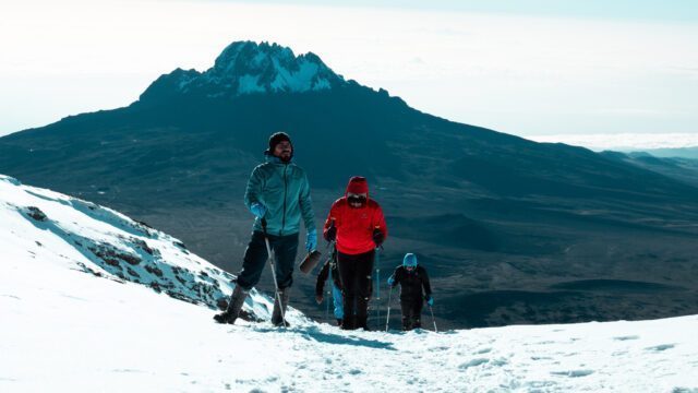 The Life Happens Outdoors team reaching Stella Point after daybreak, with the Mawenzi Crater, Kilimanjaro's second highest crater, dominating the skyline in the background during the Climb Kilimanjaro Expedition.