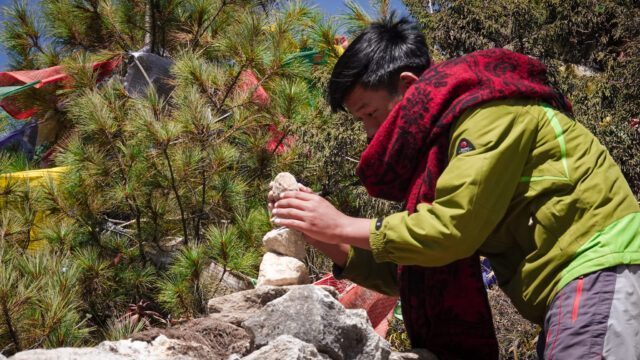 A Sherpa boy placing a rock on a cairn above Namche Bazaar during the Everest Base Camp Trek with the Life Happens Outdoors team.