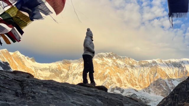 LHOer watching the sunrise on the South Face of Annapurna, deep within the Annapurna Sanctuary, with prayer flags around the stupa during the Annapurna Base Camp Trek with the Life Happens Outdoors team.