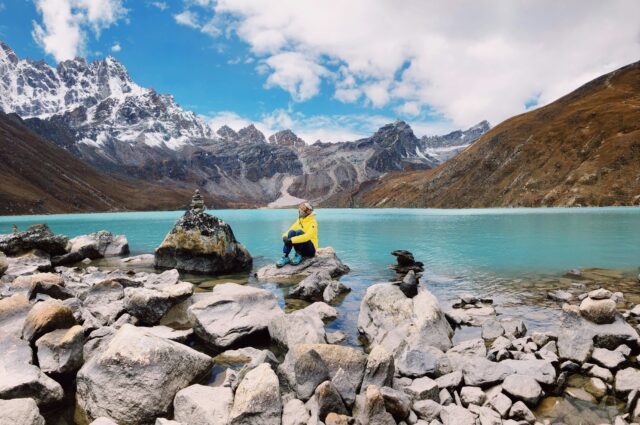 Hiker sits across the Gokyo Lakes under perfect blue skies