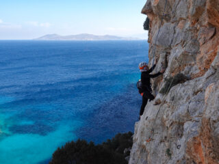 Life Happens Outdoors climber moving across textured limestone on a Kalymnos sea cliff with the Aegean Sea below.
