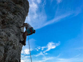 Life Happens Outdoors rock climber ascending a limestone face in Kalymnos, Greece under a bright blue sky.
