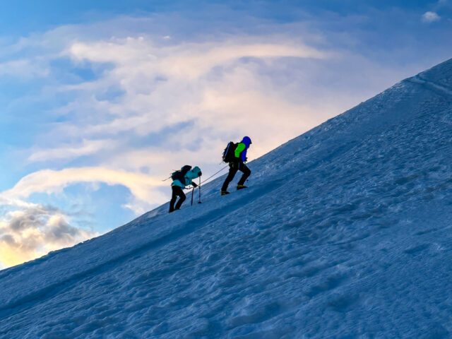 IFMGA guide Philippe Genin leading the first Emirati woman to summit Mont Blanc, Fatima Sajwani, on the first mogul of Mont Blanc at sunrise, with an incredible sky in the background during the Mont Blanc Summit Course with the Life Happens Outdoors team.