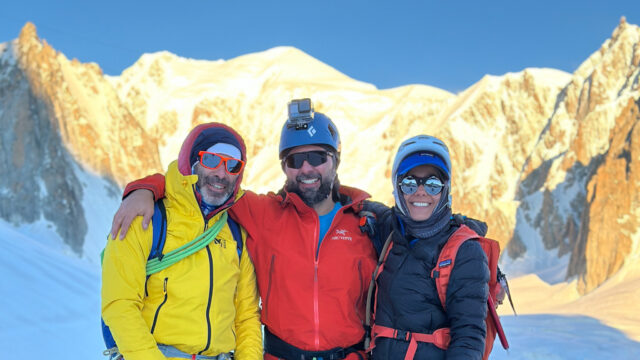 LHO guide Babis Marinidis on the summit of Petite Flambeau with Mont Blanc in the background during the Mont Blanc Summit Climb course with the Life Happens Outdoors team.