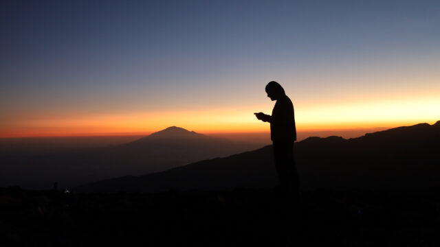 LHO team member watches the sunset from Shira Camp on the Machame Route with Mount Meru visible in the distance during a Kilimanjaro climb.