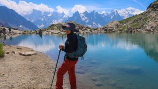 Life Happens Outdoors trekker standing at Lac Blanc on day one of the Tour du Mont Blanc hike, with the Mont Blanc summit and full Mont Blanc massif visible across the valley under a clear blue sky.