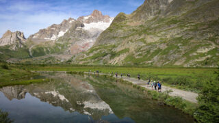 Life Happens Outdoors group hiking past alpine lakes in Italy's Val Veny on the Tour du Mont Blanc route to Col de la Seigne under clear blue skies