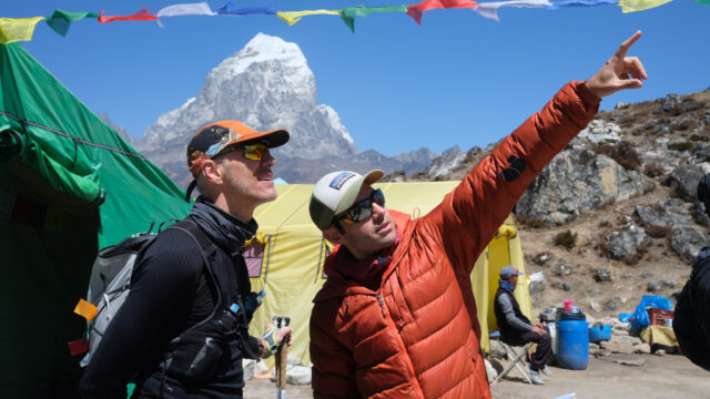 Rami Rasamny at Ama Dablam Base Camp explaining mountain conditions to a visiting trail runner amid uncertain weather and climbing delays.