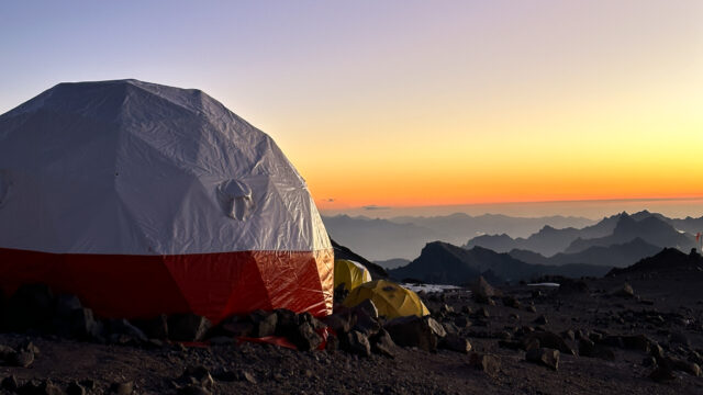 Dome tent at Aconcagua Camp 2 glowing under a golden sunset sky during a Life Happens Outdoors expedition on the Normal Route climb of Mount Aconcagua.