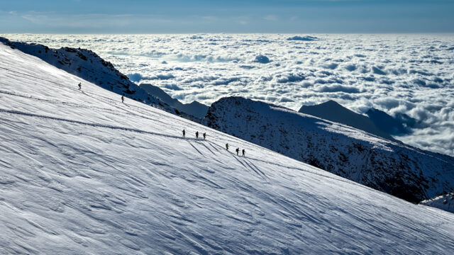 LHO climbers descending Monte Rosa in clear weather, silhouetted against a vast sea of clouds filling the valley below, showcasing an epic alpine landscape.