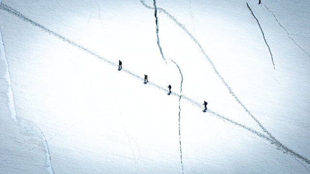Life Happens Outdoors team members trekking across a vast glacier on the Spaghetti Tour with snow-covered alpine peaks rising in the distance