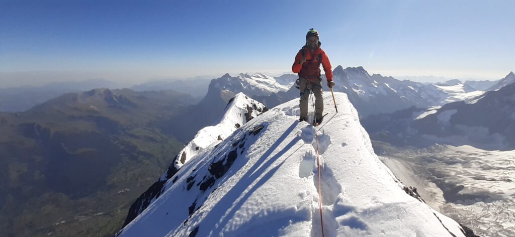 Jean Louis Moukarzel of Life Happens Outdoors standing triumphantly on the summit of the Eiger, surrounded by breathtaking alpine views and snow-covered peaks, celebrating the culmination of his challenging ascent as recounted in the article 