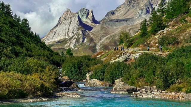 LHO group trekking through the stunning Val Veny section of the Tour du Mont Blanc, surrounded by dramatic Alpine peaks and lush green valleys, showcasing the difference between trekking and hiking.