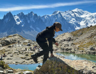 Life Happens Outdoors trekker standing at Lac Blanc on the Tour du Mont Blanc, overlooking crystal-clear waters and snow-capped peaks, highlighting the beauty of trekking in the French Alps.