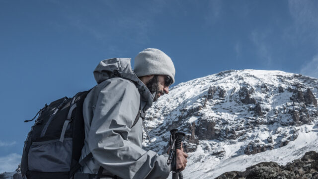 An LHO member trekking toward Barafu Camp with Mount Kilimanjaro rising in the background under clear skies during the summit approach.