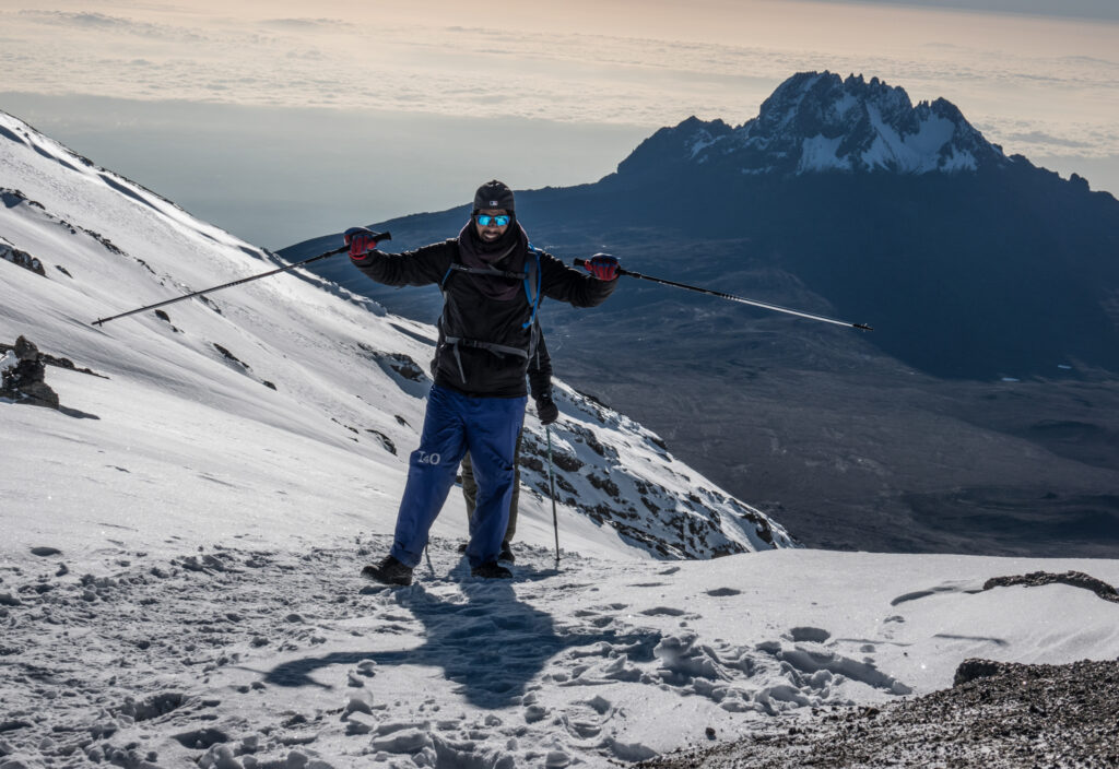 A Life Happens Outdoors community member reaching Stella Point on the Machame Route, standing at the crater rim of Mount Kilimanjaro as the sun rises above the clouds.