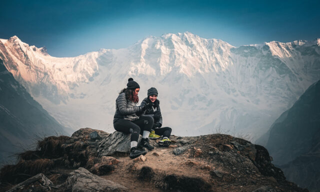 Two Life Happens Outdoors trekkers sit beneath the south face of Annapurna near Annapurna Base Camp after sunset, reflecting on the mountain landscape.