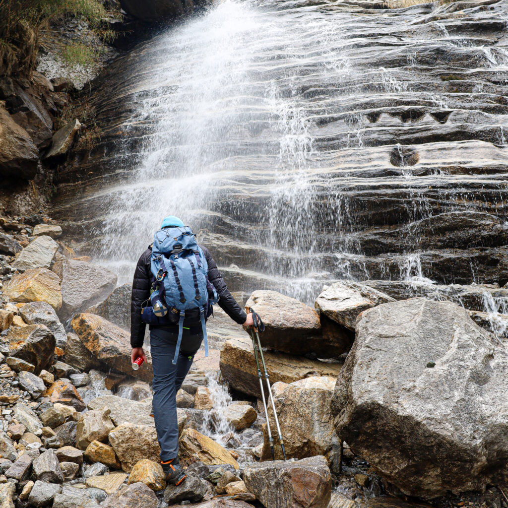 A Life Happens Outdoors community member walking near the Himalaya tea house on the Annapurna Base Camp trek, with a cascading waterfall in the background.