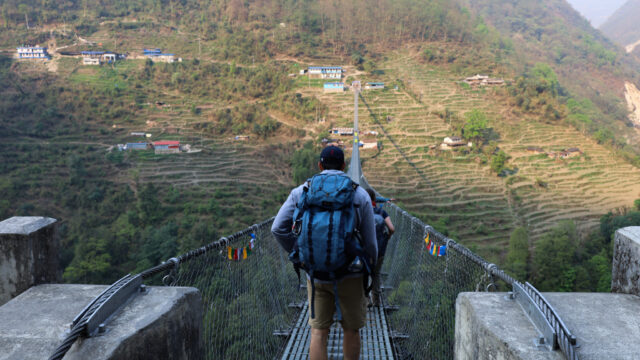 A Life Happens Outdoors community member crossing one of Nepal’s longest suspension bridges on the Annapurna Base Camp trek, surrounded by deep valleys and towering Himalayan peaks.