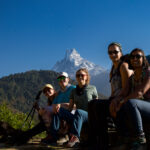 Trekker walking toward Chum Rung with Fishtail Mountain and Annapurna South rising behind under clear blue skies on the Annapurna Base Camp trail