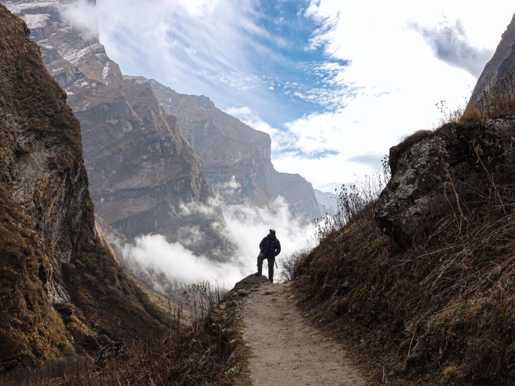 Life Happens Outdoors trekker hiking from Bamboo to Machapuchare Base Camp on the Annapurna Base Camp trek, surrounded by dramatic mountain walls and clouds rising through the valley.