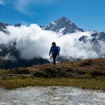Team member hiking on the Aiguille Rouge massif with the Mont Blanc massif emerging through clouds above Chamonix on the first day of the Tour du Mont Blanc.