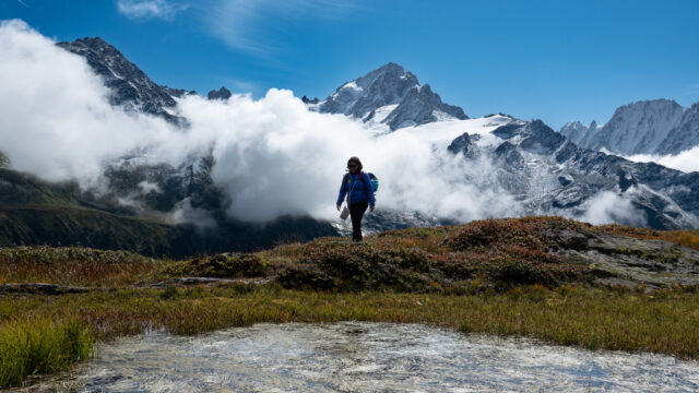 Team member hiking on the Aiguille Rouge massif with the Mont Blanc massif emerging through clouds above Chamonix on the first day of the Tour du Mont Blanc.