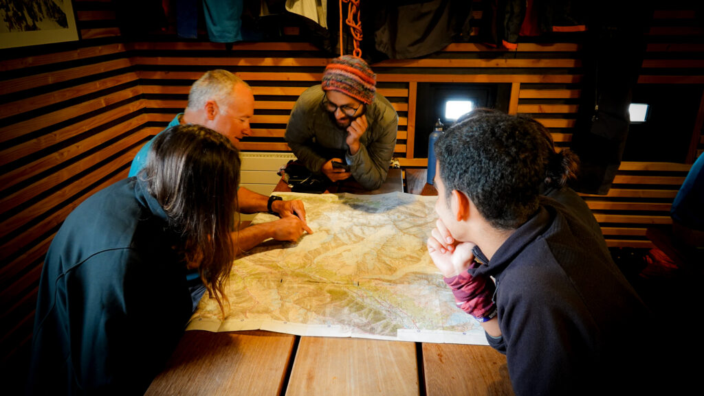 Life Happens Outdoors team gathers around the map with the guide for a Mont Blanc briefing, learning the plan, pacing, and safety for the day ahead.