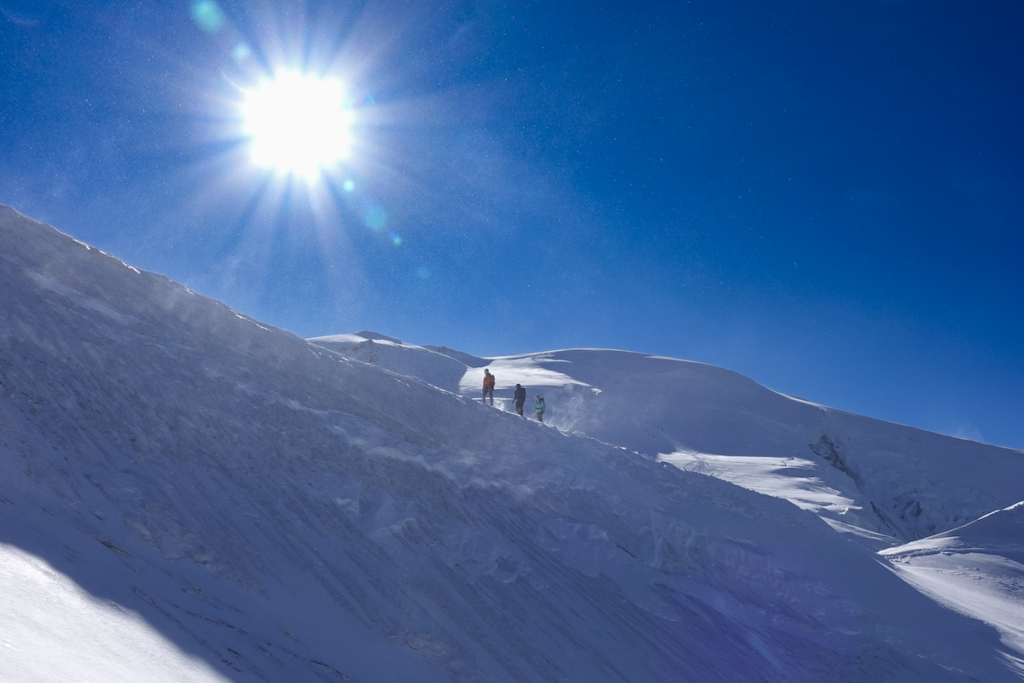 Wide angle view of Life Happens Outdoors climbers on the Dôme du Goûter with the sun in frame during a Mont Blanc climb