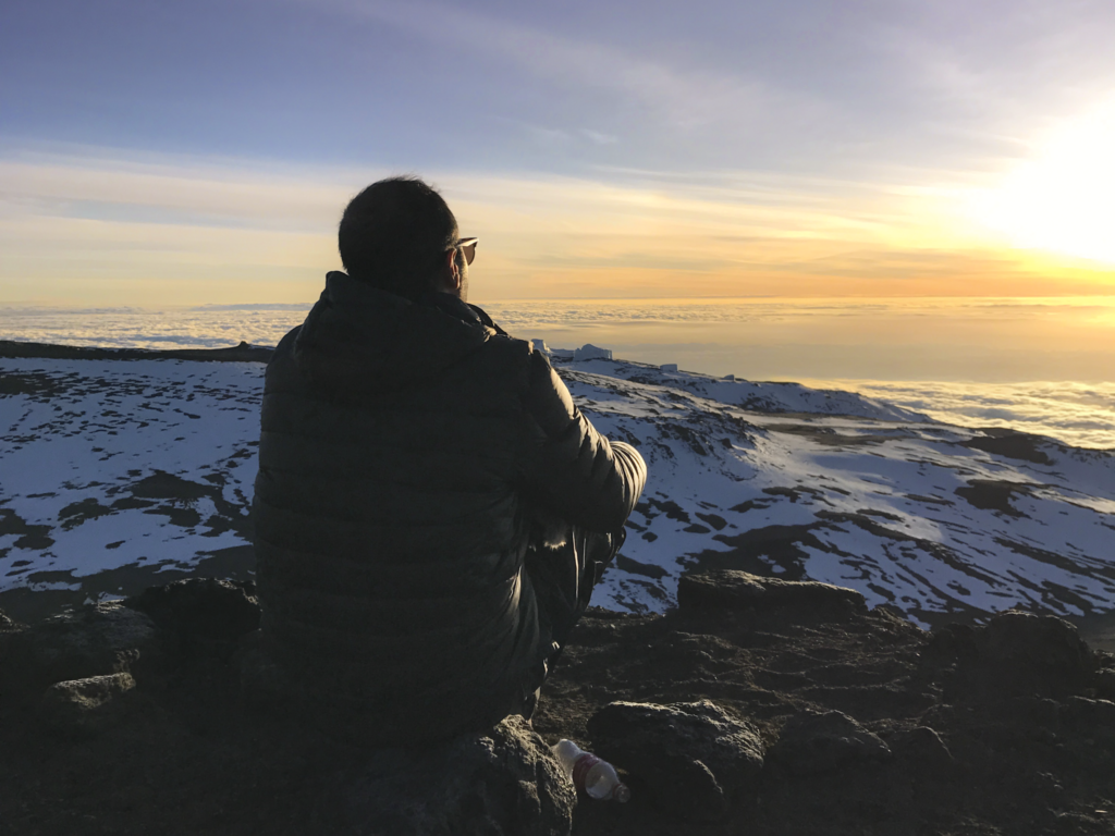 Life Happens Outdoors community member sitting on the summit of Mount Kilimanjaro at sunrise looking toward the sun