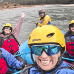 Life Happens Outdoors community members whitewater rafting in helmets and life jackets, smiling and bonding on the river