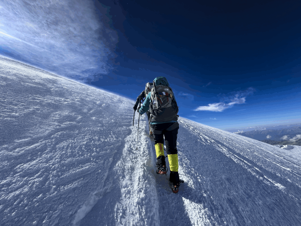 Life Happens Outdoors community member climbing a snowy mountain ridge on a high altitude expedition under a clear blue sky