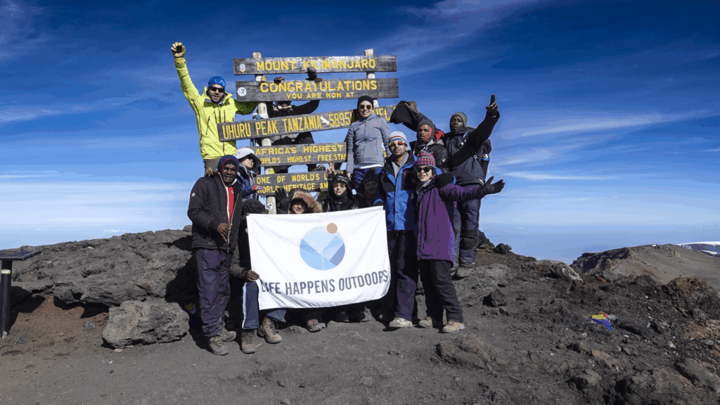 Life Happens Outdoors community members on the summit of Mount Kilimanjaro under a clear blue sky, a shared moment at the top