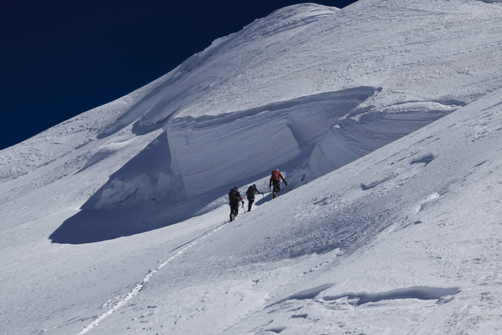 Two Life Happens Outdoors teams high on Mont Blanc, one on the third mogul and the other approaching the fourth in perfect conditions near the summit.
