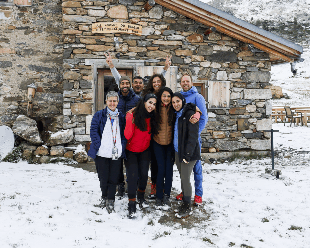 A group of Life Happens Outdoors community members stepping out from a mountain refuge into fresh snow on the Tour du Mont Blanc.