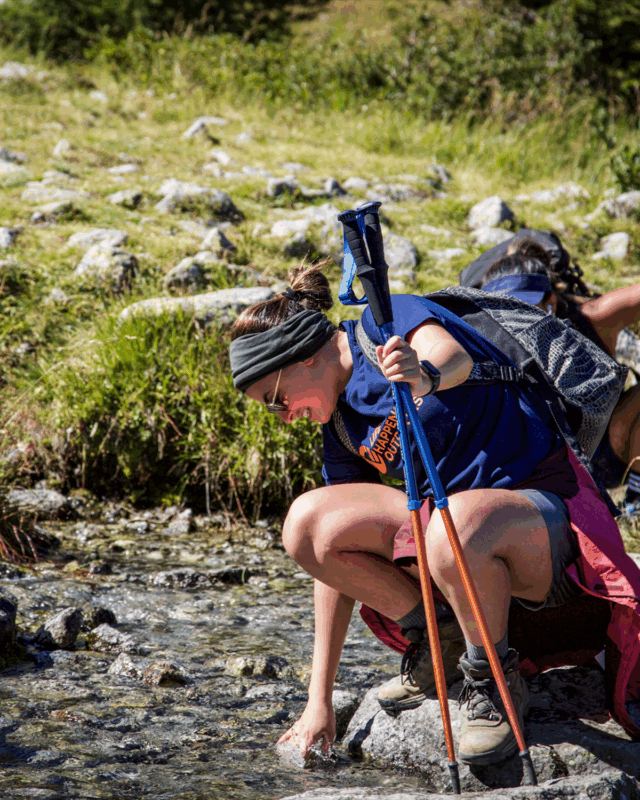 Life Happens Outdoors community member cooling her hands in a cold mountain stream during the Chamonix Valley Treks.