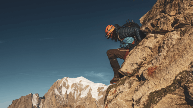 Life Happens Outdoors climber descending rocky terrain with Mont Blanc towering in the background, showing challenge and personal growth.