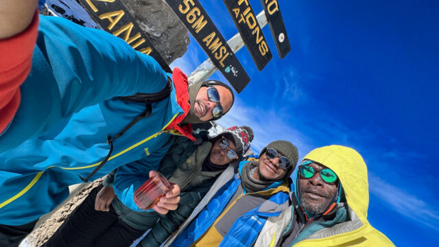 Life Happens Outdoors community members take a selfie at the Stella Point sign on the Kilimanjaro summit push moments before reaching Uhuru Peak.