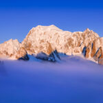 Life Happens Outdoors view of Mont Blanc above the clouds at sunrise with alpenglow, seen from the Vallée Blanche in the French Alps.